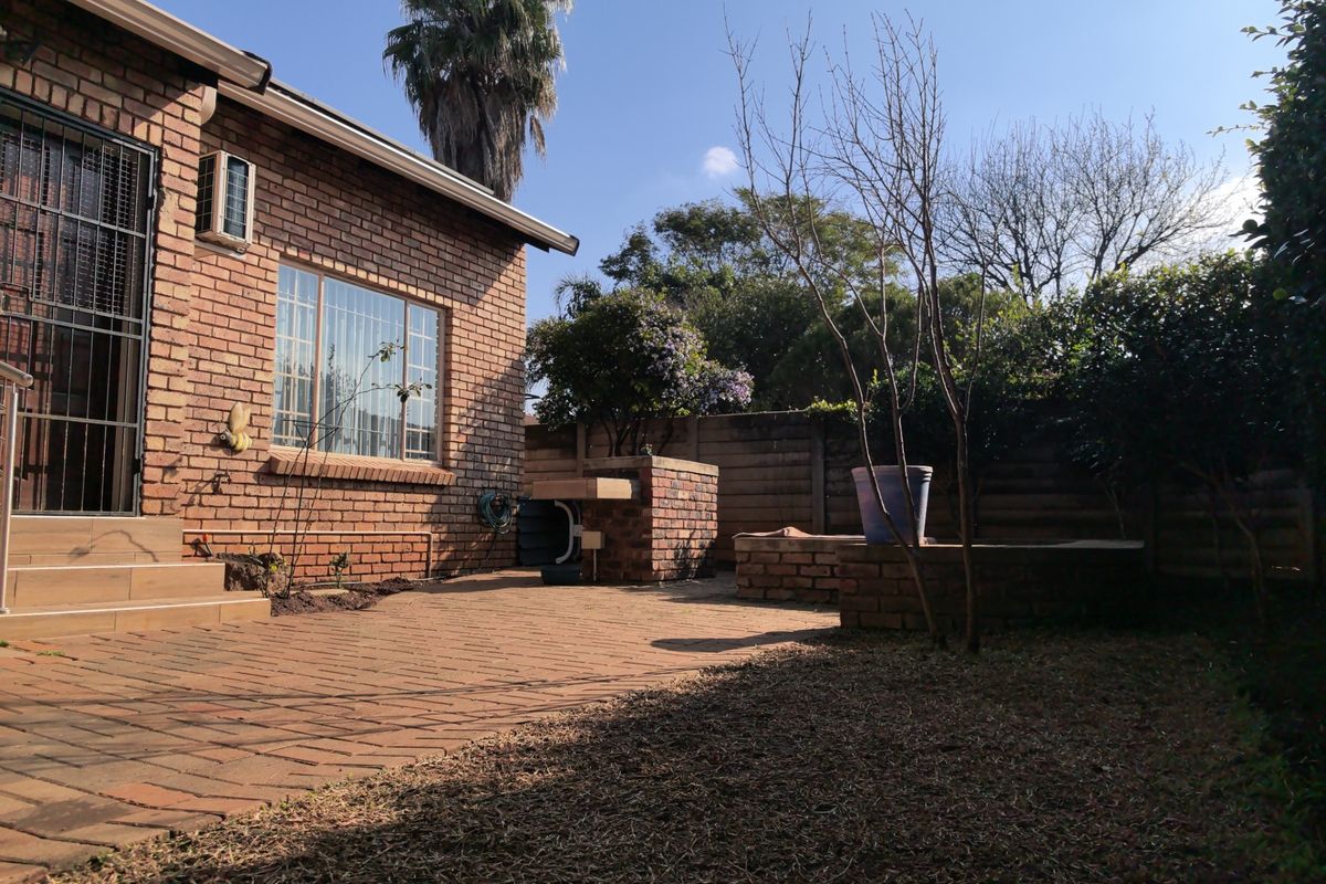 A rear exterior view of a townhouse featuring a brick facade, paved patio area, and a built-in brick braai structure within a private garden.