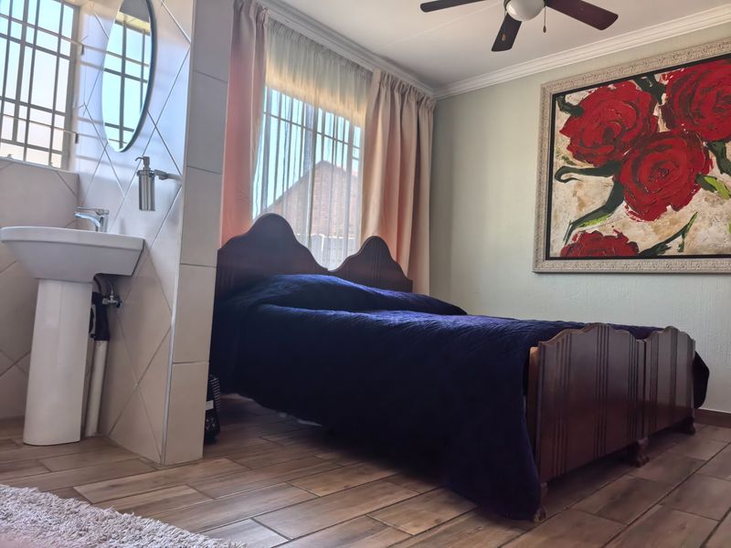 A bedroom featuring a pedestal washbasin integrated into a tiled partition wall, wood-look tiled flooring, and a ceiling fan.
