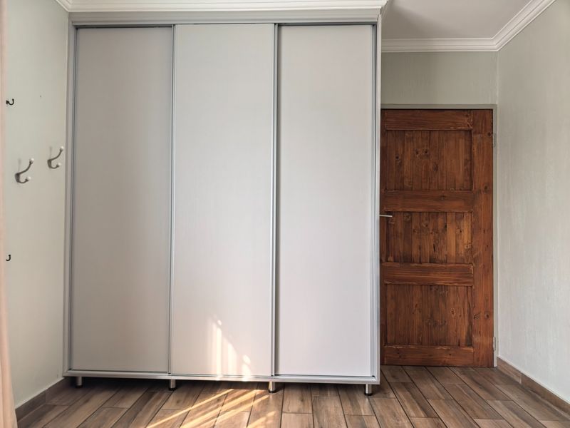 A bedroom featuring a large built-in sliding door wardrobe, wood-look tile flooring, and a rustic timber door.