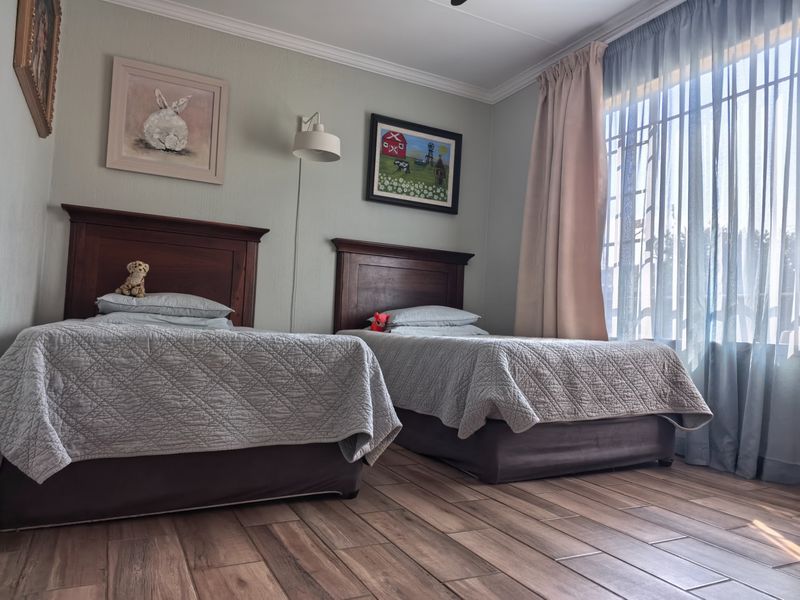 A well-maintained bedroom featuring tiled flooring, coving, and a wall-mounted light fixture, with natural light entering through a large window.