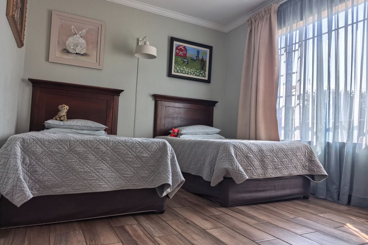 A well-maintained bedroom featuring tiled flooring, coving, and a wall-mounted light fixture, with natural light entering through a large window.