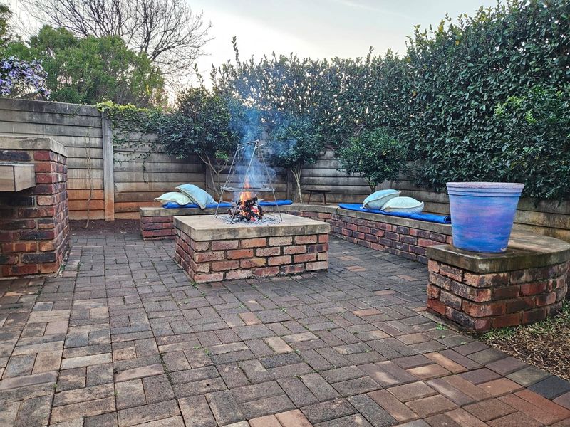 Outdoor patio area featuring a built-in brick fire pit and integrated brick bench seating, surrounded by a privacy hedge and concrete boundary wall.