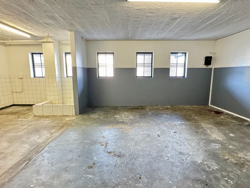 An open-plan industrial utility space featuring concrete flooring, fluorescent lighting, and a dedicated tiled wash area with security-barred windows.