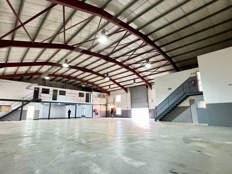 Spacious industrial warehouse featuring a high-clearance steel portal frame, concrete flooring, mezzanine level with staircase, and a large roller shutter door for easy access.