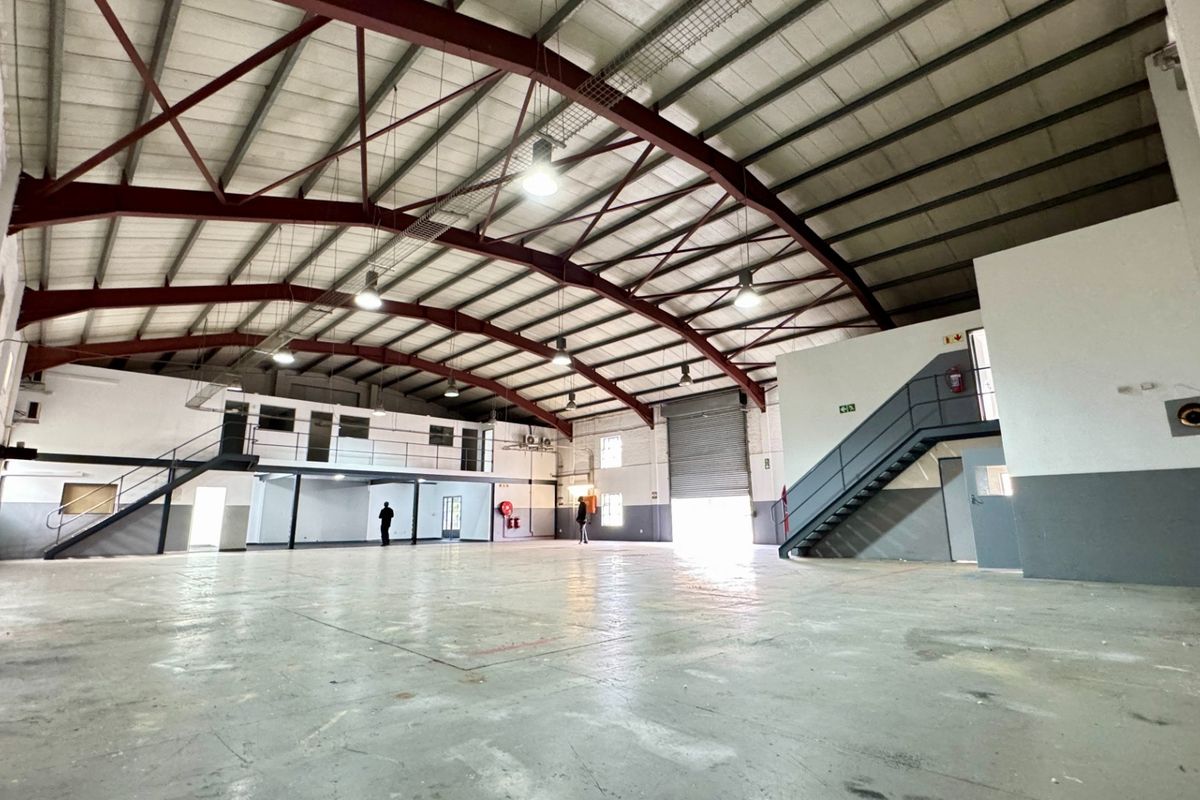 Spacious industrial warehouse featuring a high-clearance steel portal frame, concrete flooring, mezzanine level with staircase, and a large roller shutter door for easy access.