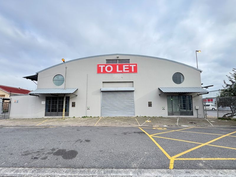Front elevation of an industrial warehouse featuring a large central roller shutter door, metal awnings, and dedicated paved parking area.