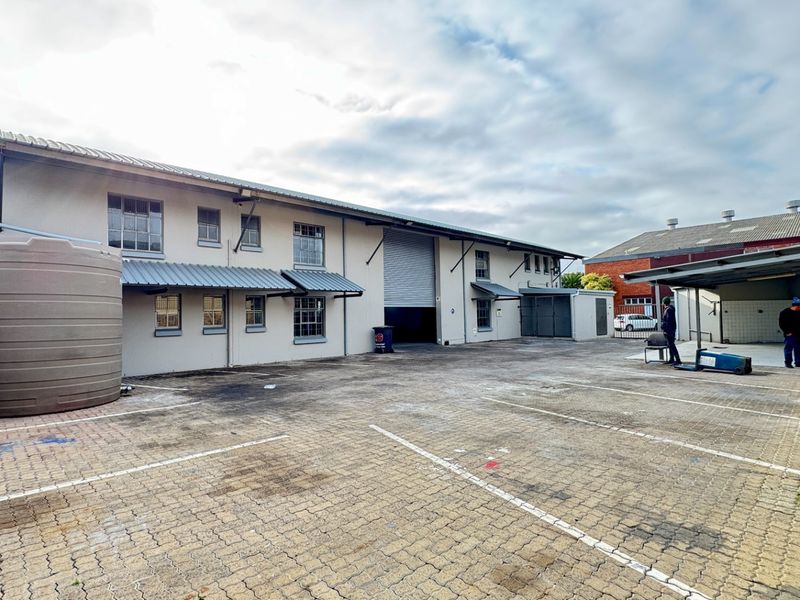 Rear industrial yard featuring a large paved area, water storage tank, covered loading bay, and roller shutter access to the main warehouse building.