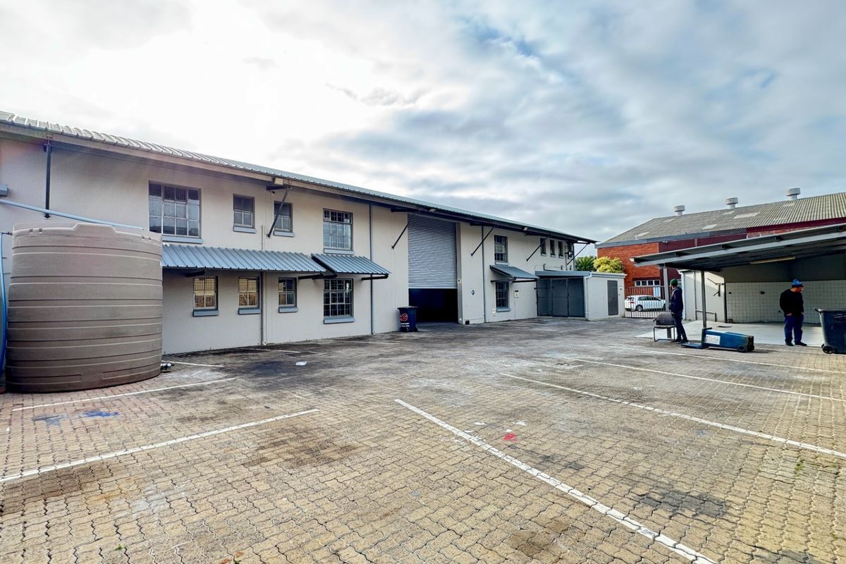 Rear industrial yard featuring a large paved area, water storage tank, covered loading bay, and roller shutter access to the main warehouse building.