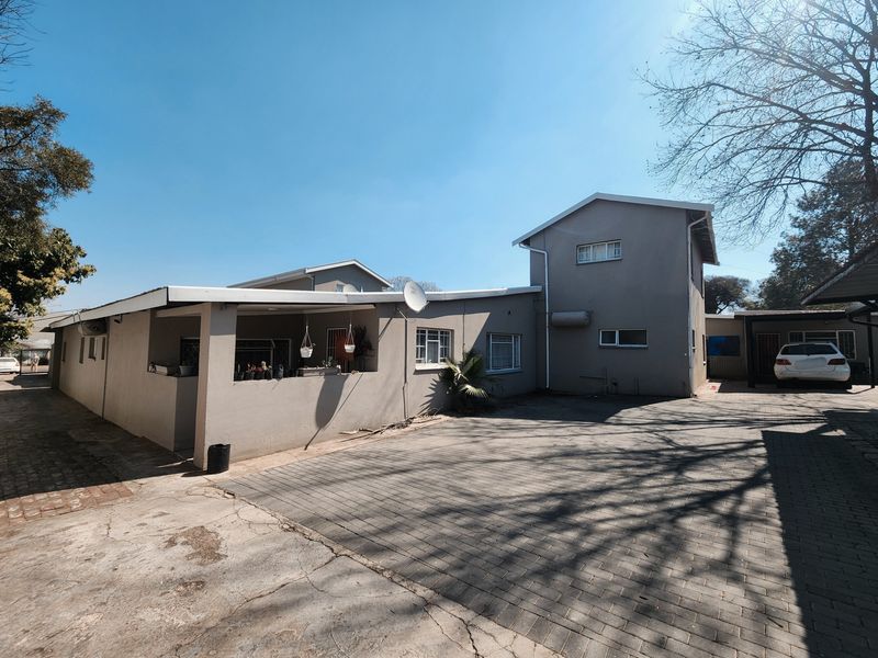A view of the front exterior featuring a paved driveway, covered patio area, and multi-level building structure with security bars on windows.