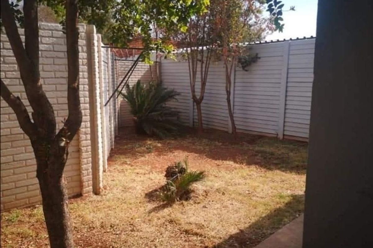 A private rear garden area enclosed by precast concrete and brick boundary walls, featuring established trees and dry lawn space.