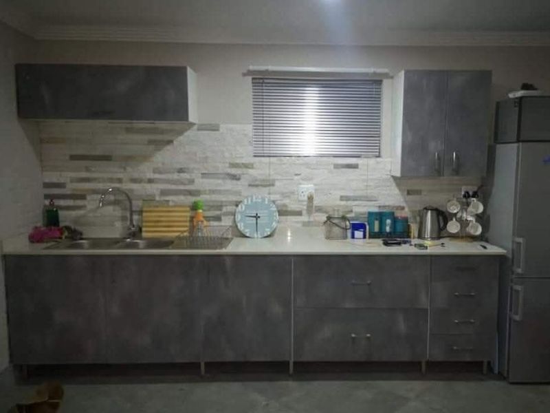 A functional kitchen featuring modern grey cabinetry, stone countertops, a double sink, and a textured stone tile backsplash.