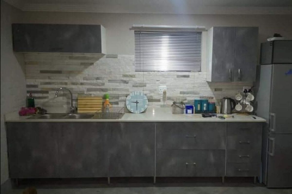 A functional kitchen featuring modern grey cabinetry, stone countertops, a double sink, and a textured stone tile backsplash.