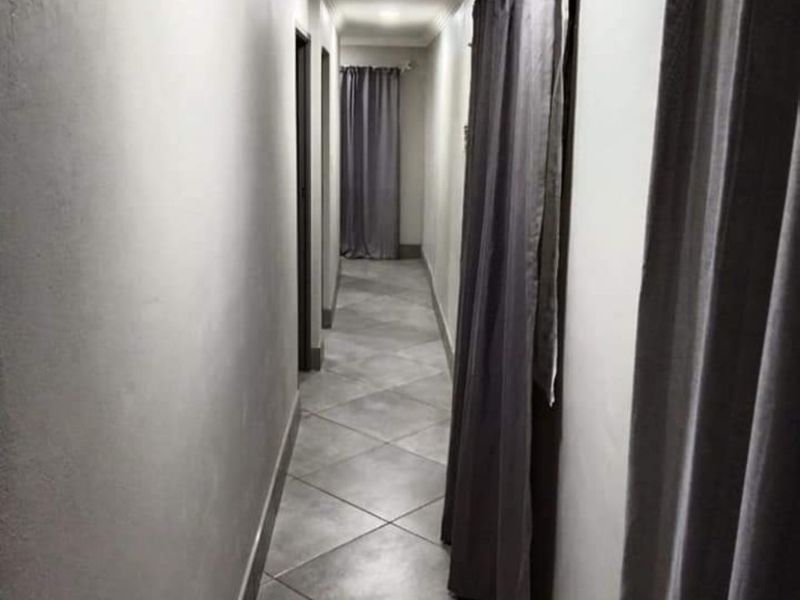 A narrow residential hallway featuring neutral tiled flooring, recessed downlighting, and decorative cove cornicing.