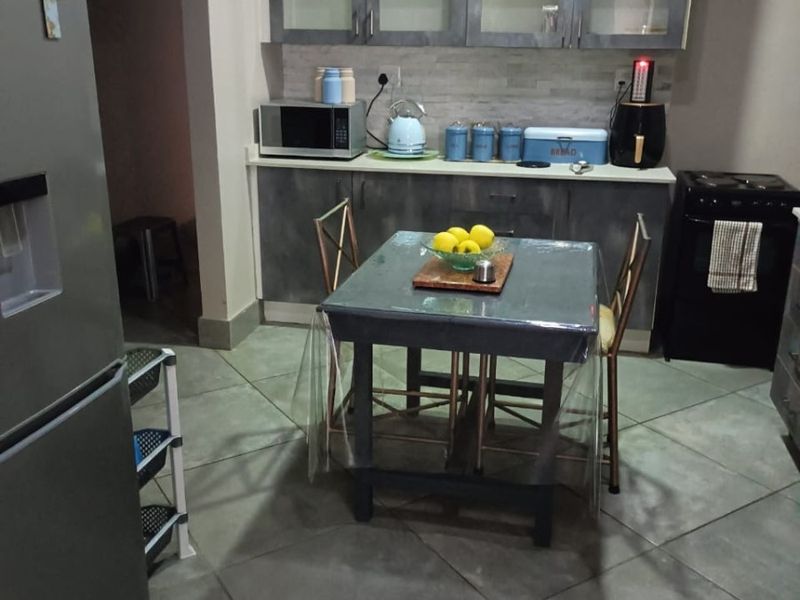 A functional kitchen featuring grey-toned cabinetry, glass-front upper storage, a stone-look backsplash, and large format floor tiles.