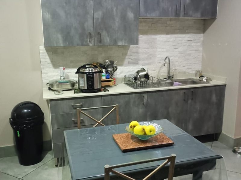 A compact kitchen featuring grey cabinetry, a stone tile backsplash, and a stainless steel sink, complemented by tiled flooring.