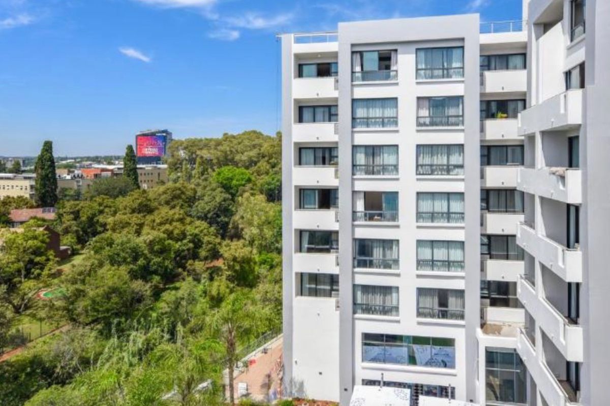 Exterior view of the modern apartment building facade featuring multiple levels of balconies and large windows overlooking a green landscape.