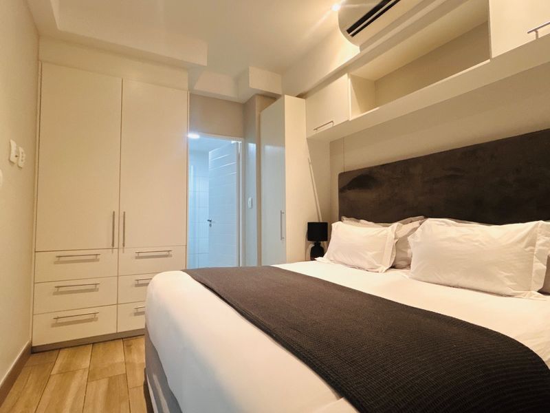A well-appointed bedroom featuring extensive built-in cabinetry, overhead storage, integrated air conditioning, and modern wood-look tile flooring.