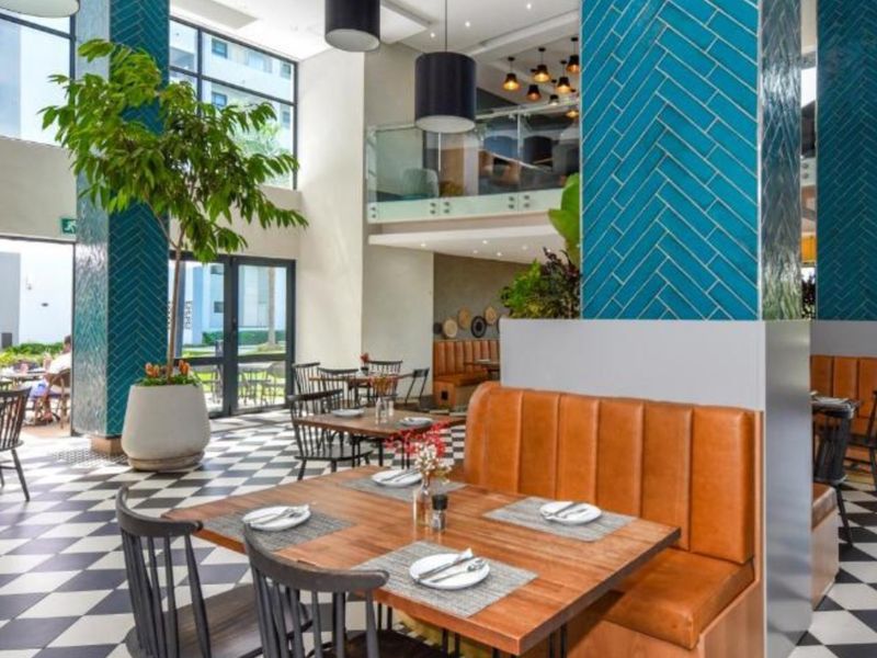 Modern clubhouse area featuring high ceilings, mezzanine level, striking herringbone tiled columns, and large windows overlooking the exterior grounds.