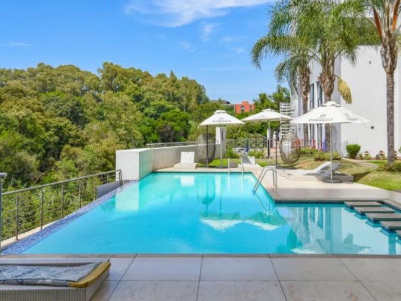 A well-maintained infinity edge swimming pool featuring a tiled deck, stepping stones, and a stainless steel balustrade overlooking a lush green landscape.