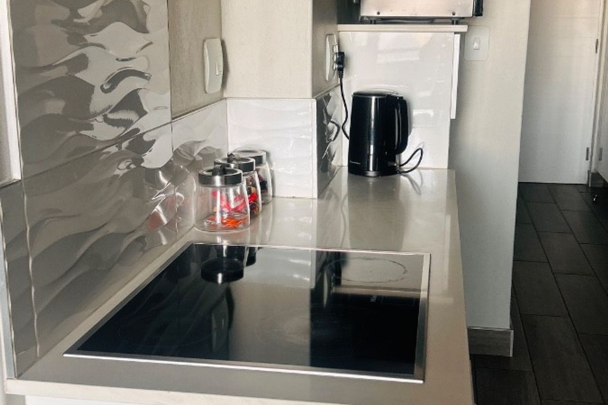 Compact modern kitchen featuring a sleek induction hob, integrated extractor fan, stone countertops, and contemporary tiled backsplash.