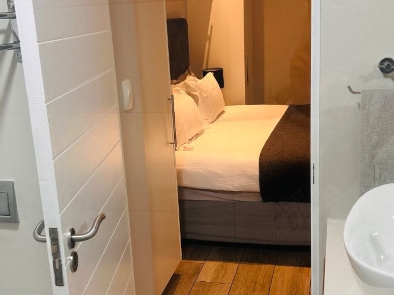 A view from the bathroom into a compact, well-maintained bedroom featuring built-in cupboards, air conditioning, and modern wood-look tile flooring.