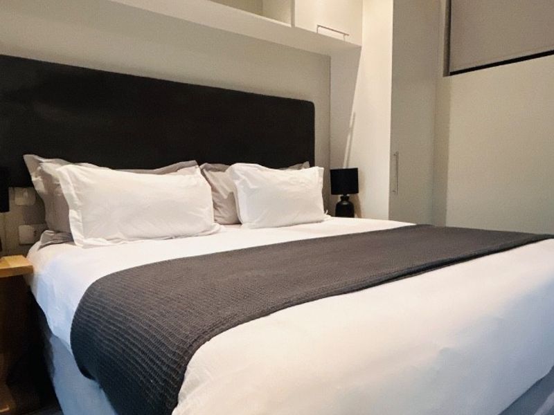 A well-maintained bedroom featuring built-in overhead storage, integrated wardrobe cabinetry, and a wall-mounted split-system air conditioning unit.