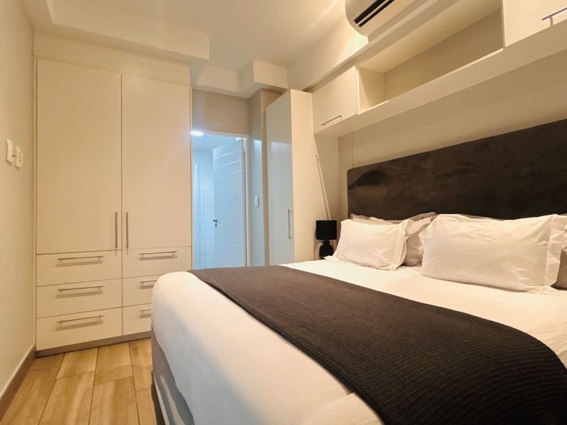 A well-maintained bedroom featuring extensive built-in cabinetry, overhead storage, and an integrated air conditioning unit with modern wood-look flooring.