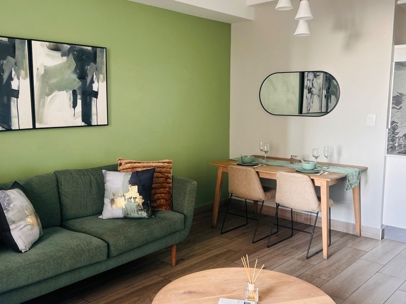 A bright open-plan living and dining area featuring modern laminate flooring, a vibrant accent wall, and a compact, well-integrated kitchen space.