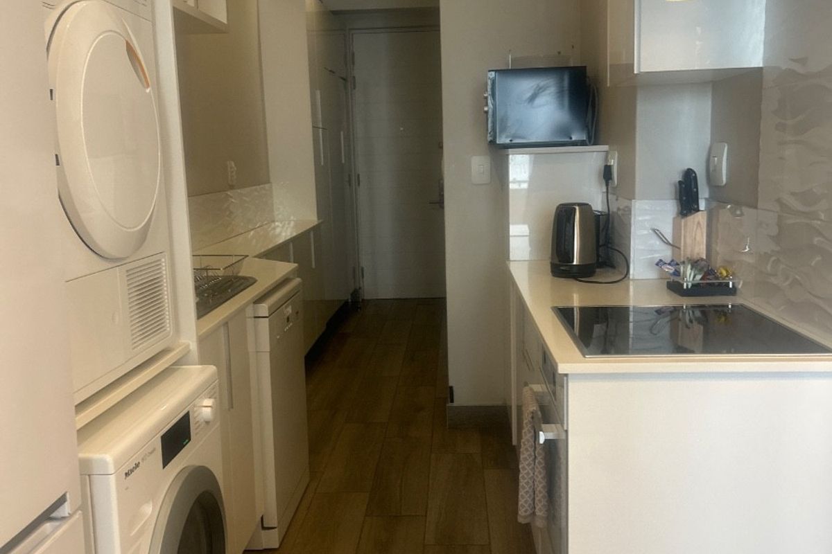 A compact, modern kitchen featuring white cabinetry, integrated laundry appliances, an electric hob with extractor fan, and wood-look tiled flooring.