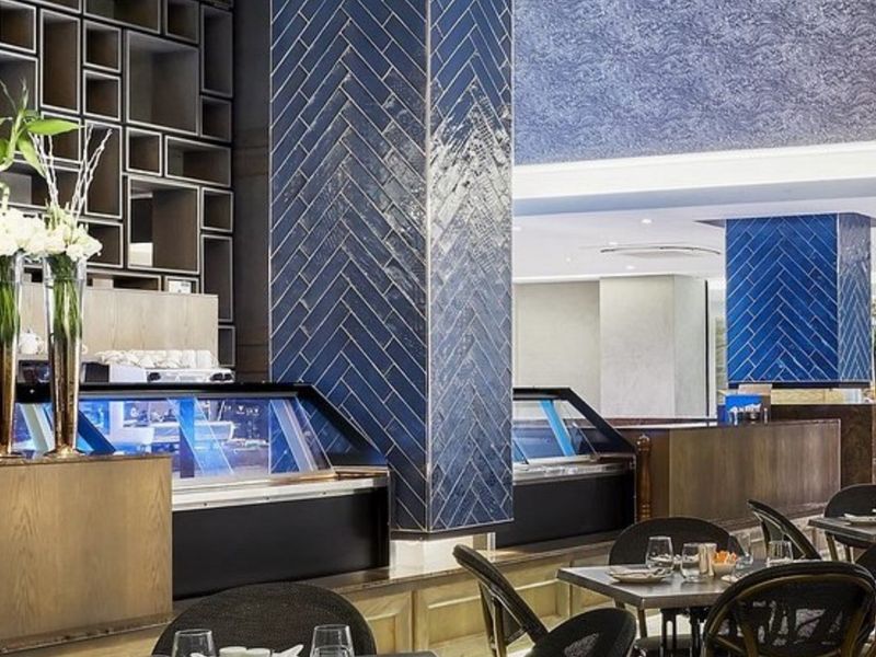 A sophisticated bar area featuring striking blue herringbone tiled columns, integrated refrigerated display counters, and custom built-in shelving with modern recessed lighting.