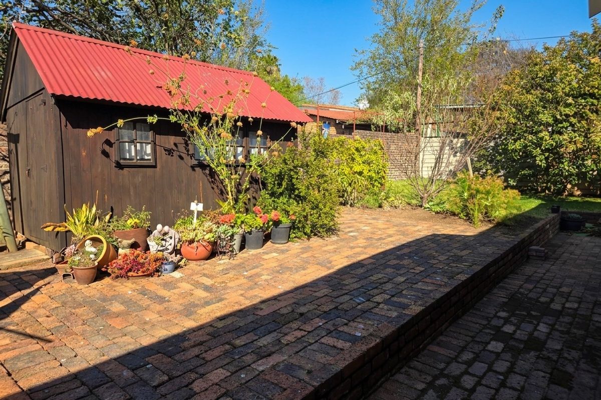 A rear garden area featuring brick paving, a raised retaining wall, and a timber shed with a red corrugated metal roof.