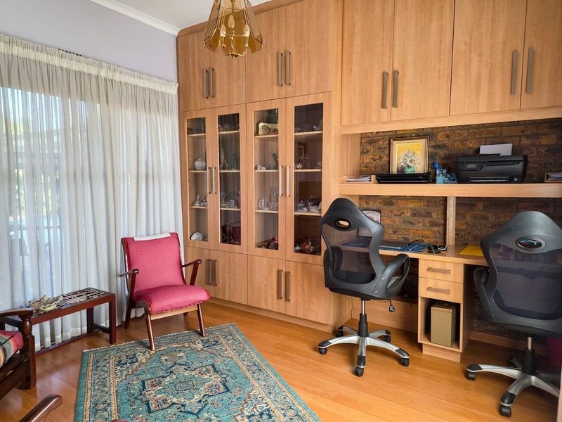 A functional home office featuring extensive built-in wooden cabinetry, a dedicated desk workspace, and an exposed brick feature wall.