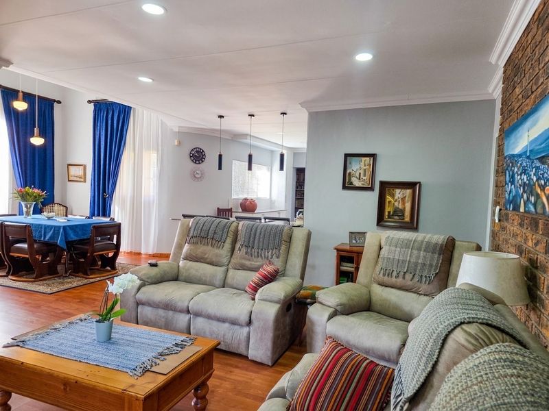 Spacious open-plan living and dining area featuring warm laminate flooring, recessed lighting, and a distinctive exposed brick feature wall.