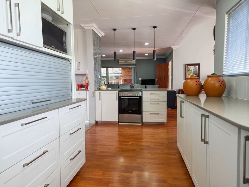 Modern kitchen featuring white cabinetry, stone countertops, integrated microwave, and a freestanding oven, flowing into an open-plan living area with warm laminate flooring.