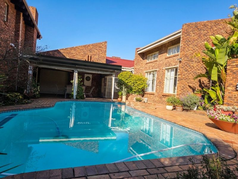 A well-maintained swimming pool area featuring brick paving, a covered patio, and classic face brick exterior walls.