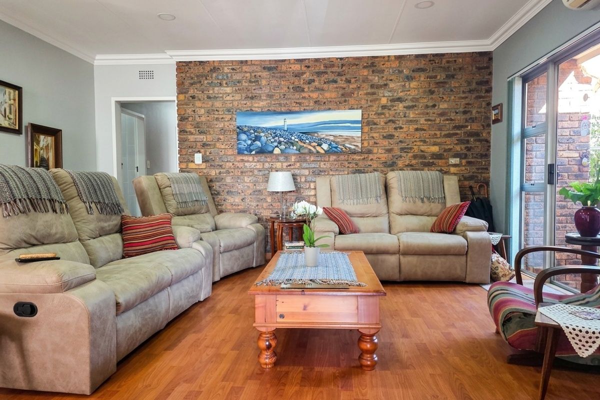 A comfortable living room featuring a prominent exposed brick feature wall, warm laminate flooring, and large sliding glass doors providing natural light.