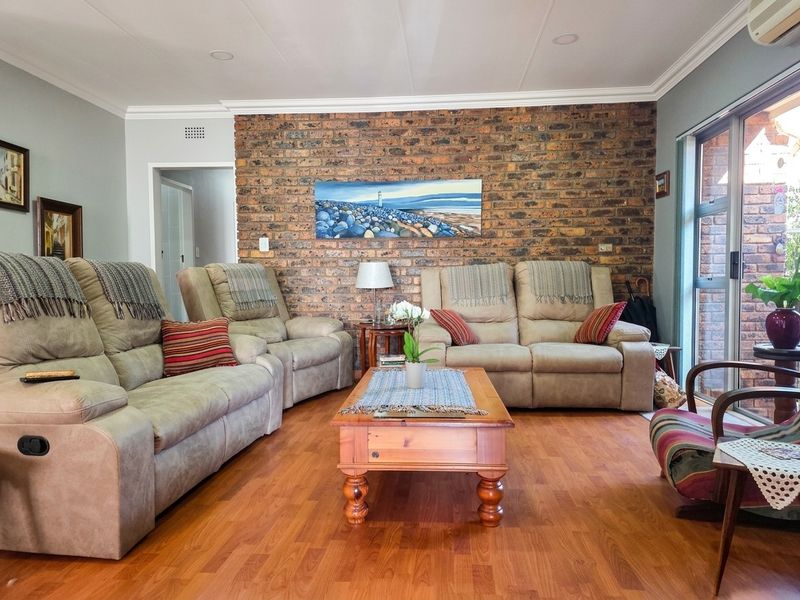 A comfortable living room featuring a prominent exposed brick feature wall, warm laminate flooring, and large sliding glass doors providing natural light.