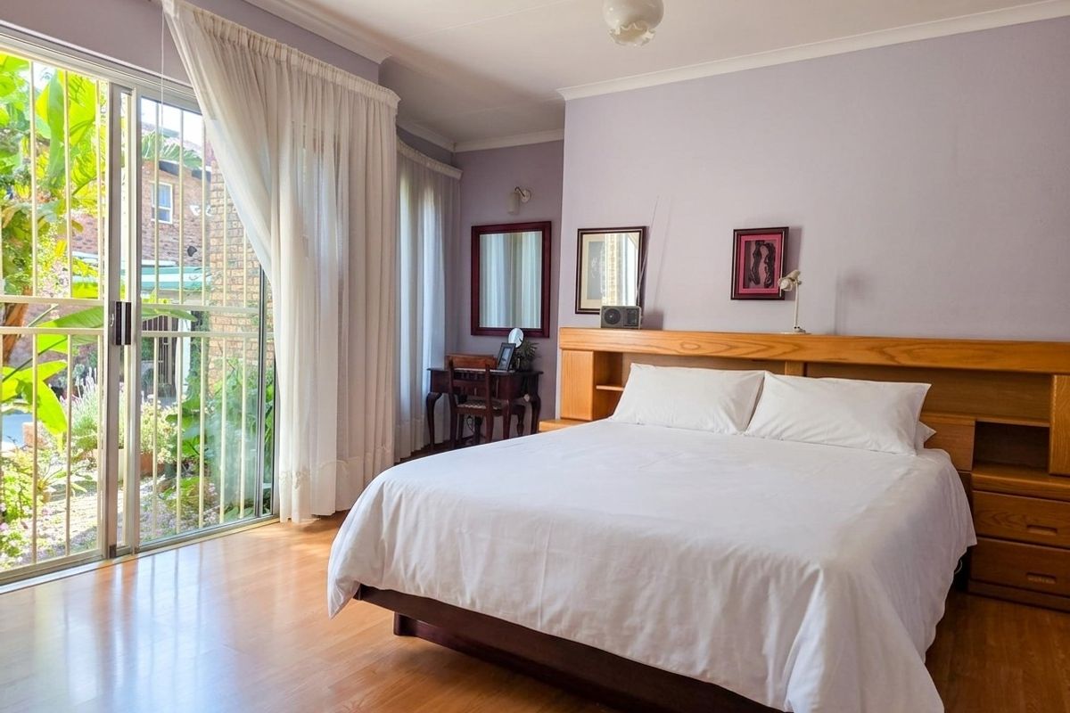 Spacious bedroom featuring laminate flooring, a built-in wooden headboard, and large sliding glass doors providing direct access to the garden area.