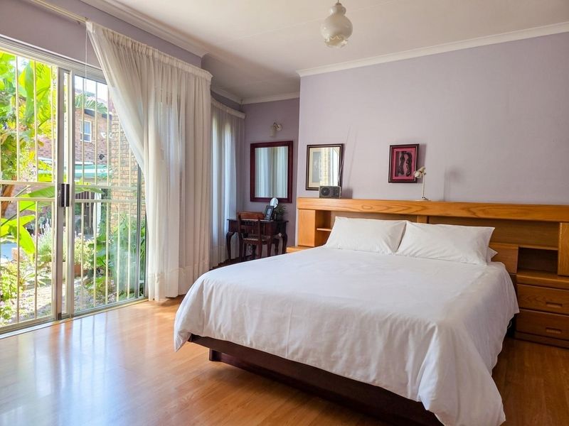 Spacious bedroom featuring laminate flooring, a built-in wooden headboard, and large sliding glass doors providing direct access to the garden area.