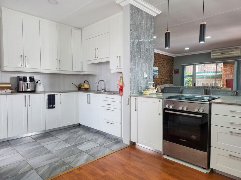 Modern kitchen featuring white cabinetry, stainless steel oven, mosaic tile accent wall, and a blend of tiled and laminate flooring with open-plan flow.