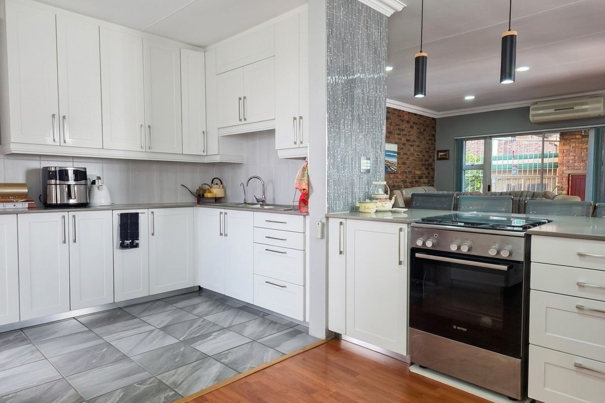 Modern kitchen featuring white cabinetry, stainless steel oven, mosaic tile accent wall, and a blend of tiled and laminate flooring with open-plan flow.