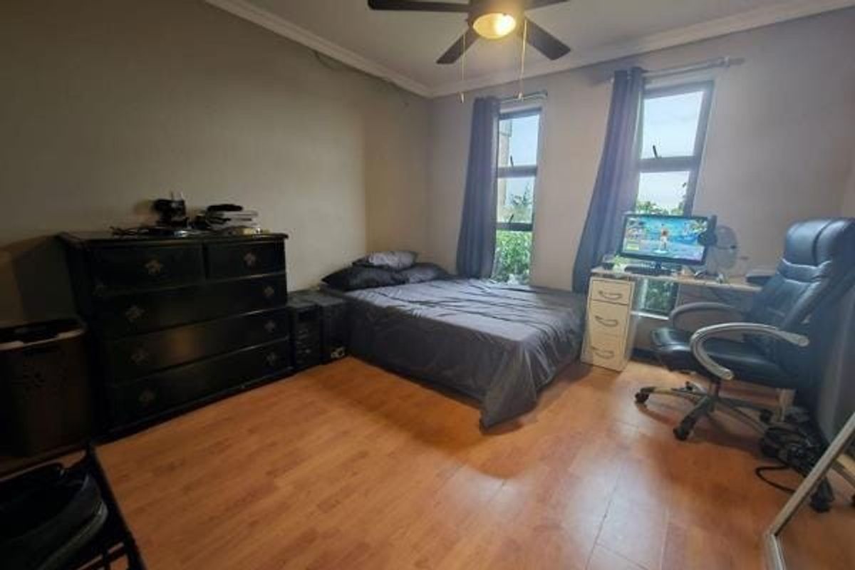 A functional bedroom featuring laminate flooring, a ceiling fan, and dual casement windows providing natural light.