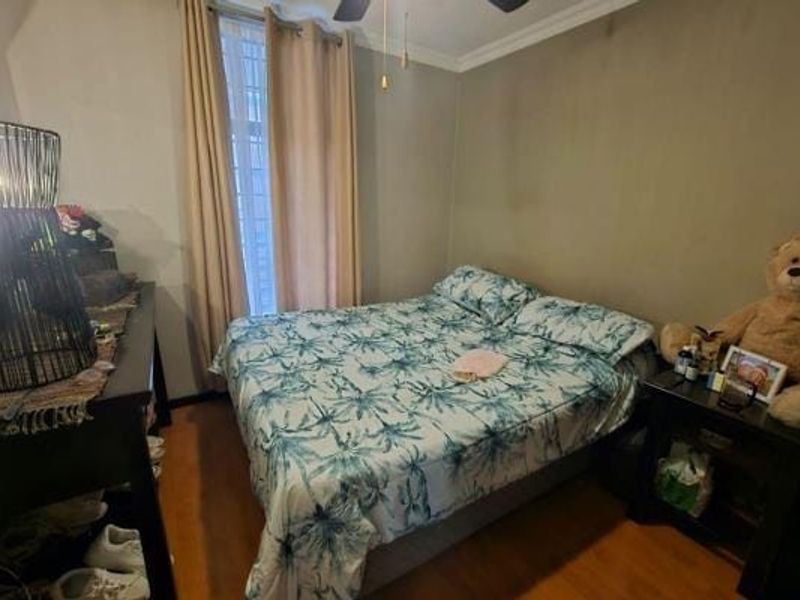 A functional bedroom featuring laminate flooring, a ceiling fan, and window security bars, providing a comfortable and secure living space.