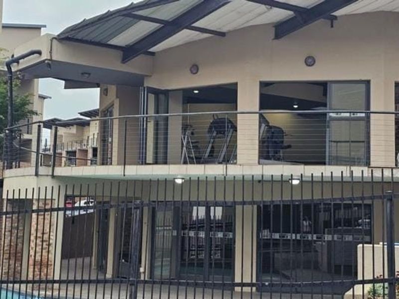 Exterior view of a multi-level apartment building featuring a balcony with steel railings, sliding glass doors, and an exposed steel roof structure.