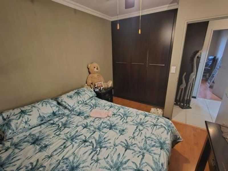 A bedroom featuring dark wood built-in cupboards, laminate flooring, and a ceiling fan, with an adjacent hallway visible.