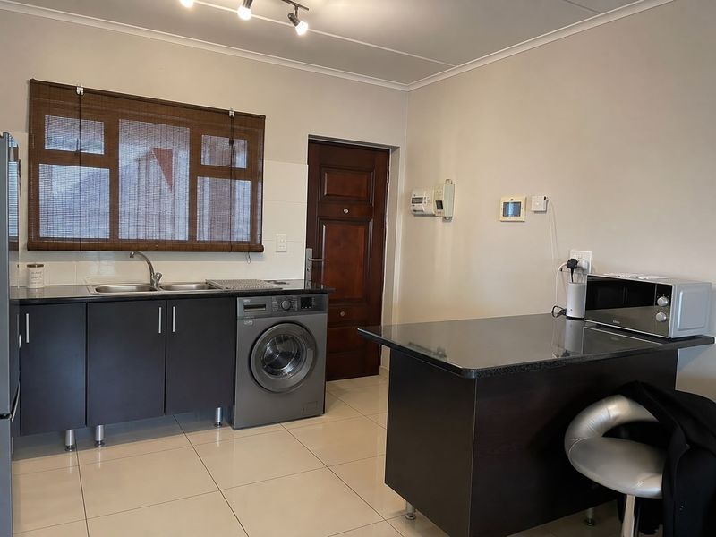 Modern kitchen featuring dark cabinetry, granite countertops, a breakfast bar, and tiled flooring with an integrated washing machine.