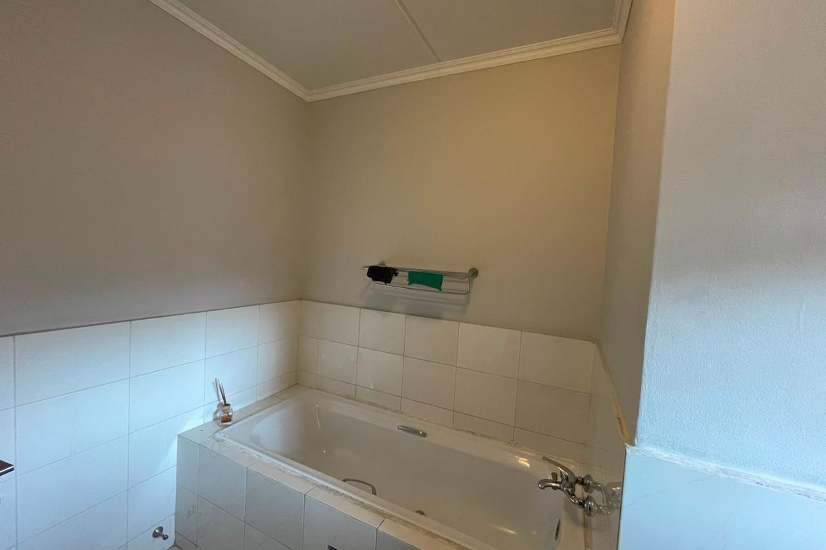 A functional bathroom featuring a built-in bathtub with tiled surround and a wall-mounted towel rail, requiring minor maintenance to the tile finish.
