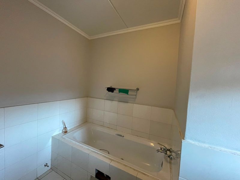 A functional bathroom featuring a built-in bathtub with tiled surround and a wall-mounted towel rail, requiring minor maintenance to the tile finish.