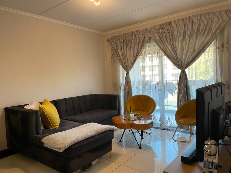 A well-maintained living room featuring polished floor tiles, neutral walls, and a large sliding glass door providing access to the balcony.