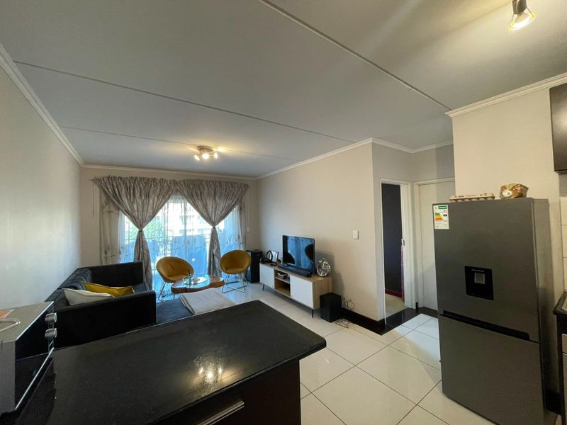 Open plan living area featuring tiled flooring, a kitchen breakfast bar, and sliding door access to a balcony, creating a bright and functional space.